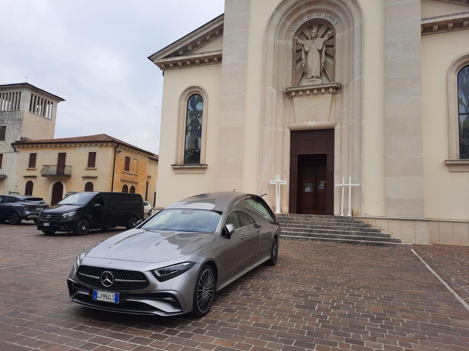 Un carro funebre argentato parcheggiato davanti a una chiesa, in preparazione per un funerale.