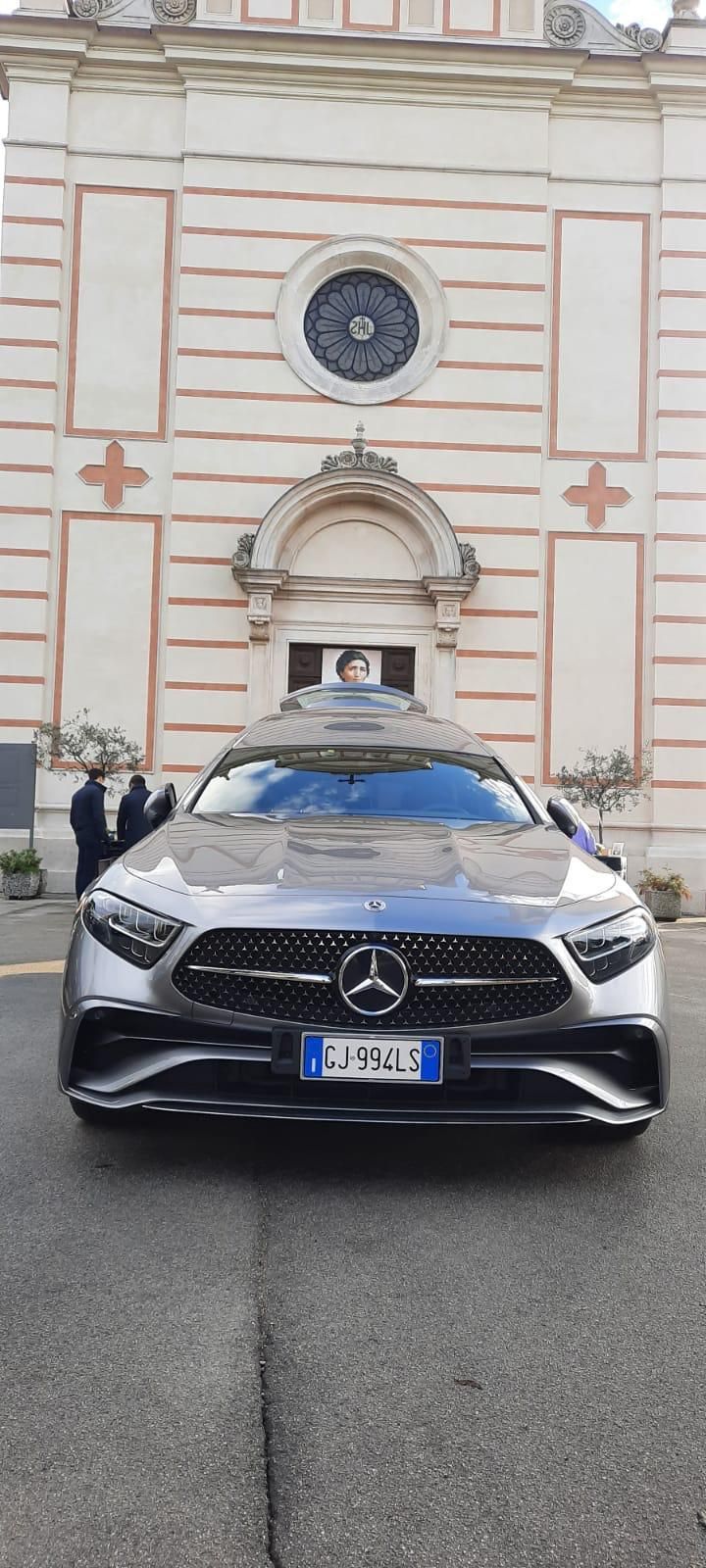 Un carro funebre Mercedes color argento parcheggiato davanti a una chiesa.