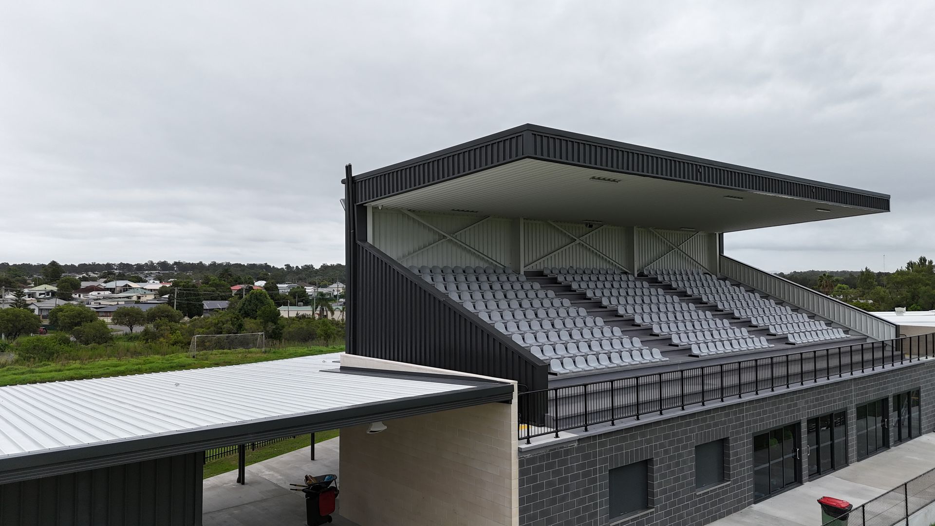 Empty stadium grandstand with gray seating and a dark roof under an overcast sky