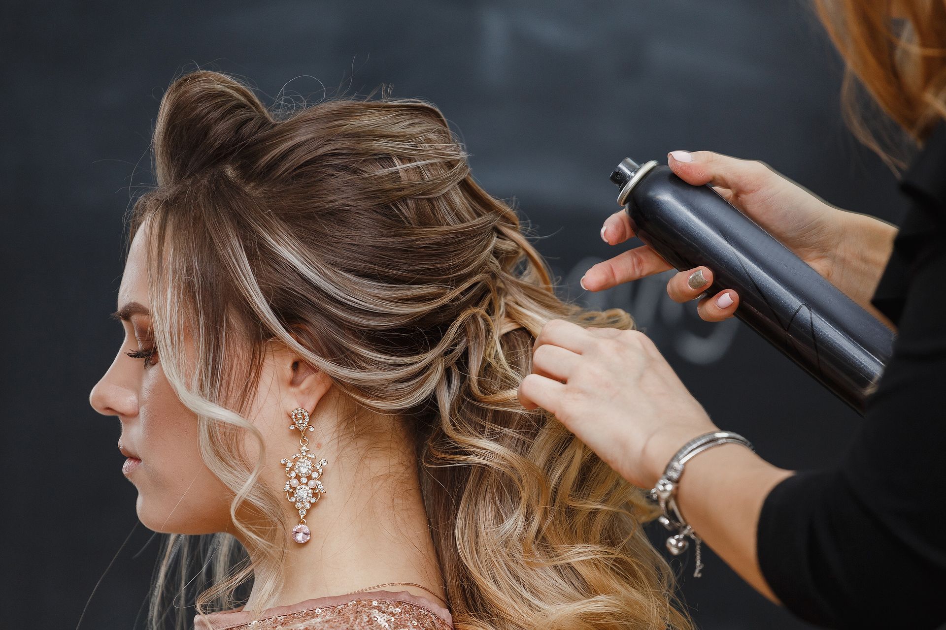 A stylist finishing blonde balayage curls with hairspray
