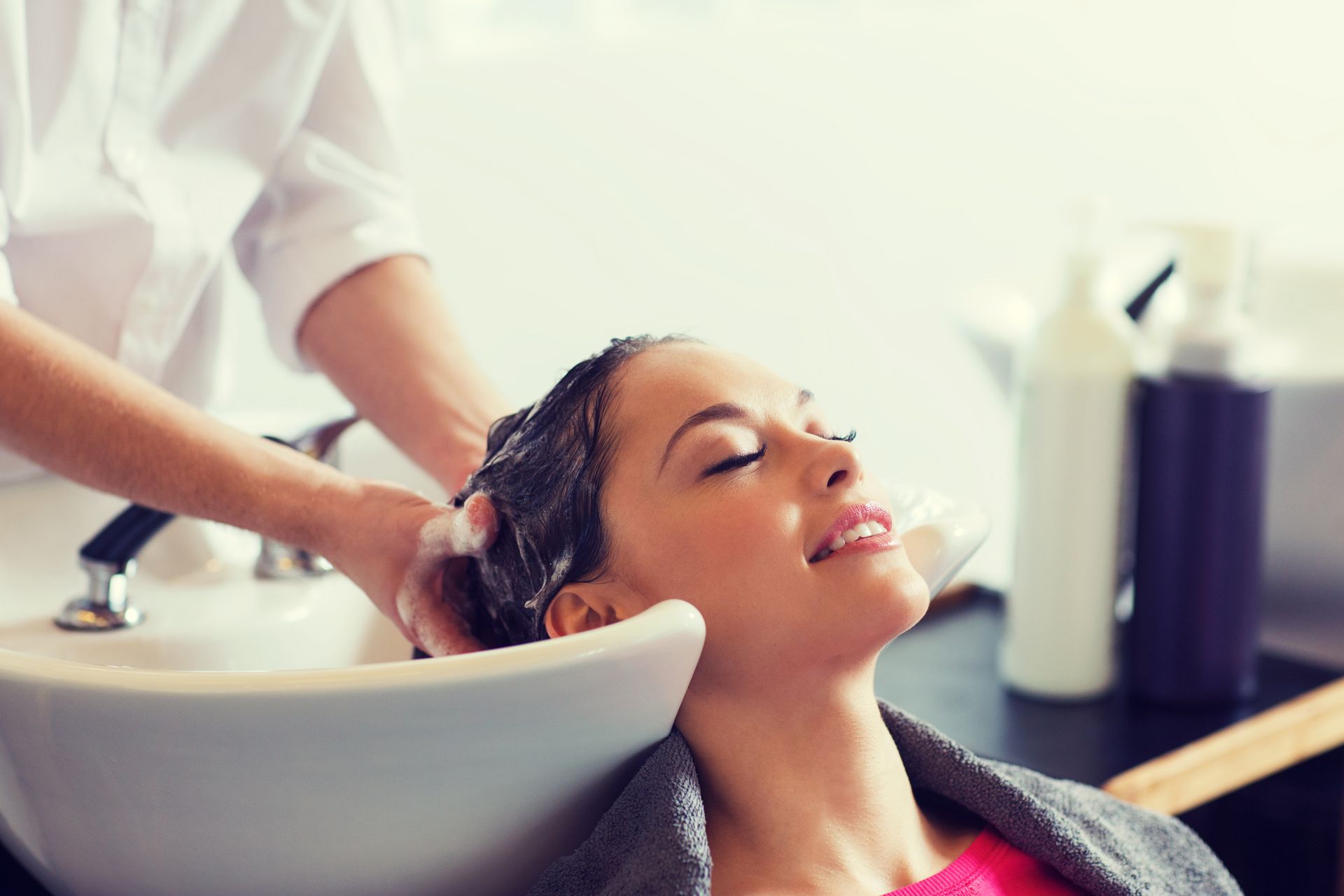 A stylist washing a smiling client's hair at a salon shampoo sink A stylist washing a smiling client's hair at a salon shampoo sink