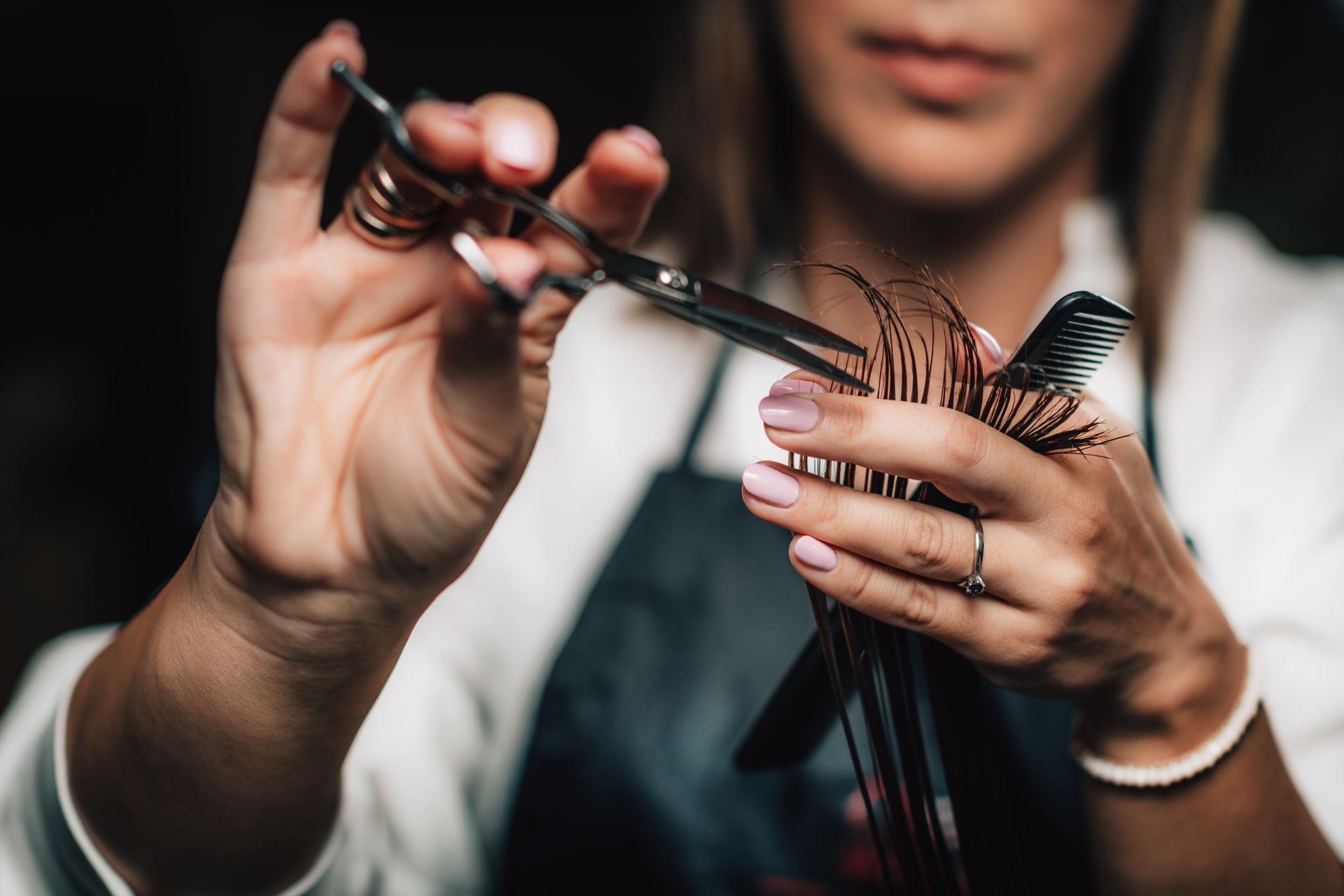 Close-up of stylist cutting hair with scissors and comb in a salon setting. Close-up of stylist cutting hair with scissors and comb in a salon setting.