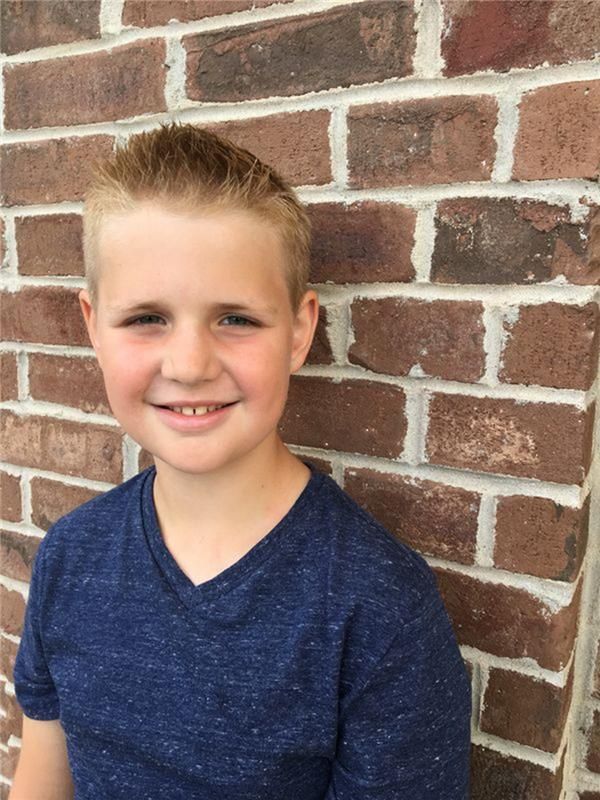 A fair-haired person smiling against a brown brick wall.