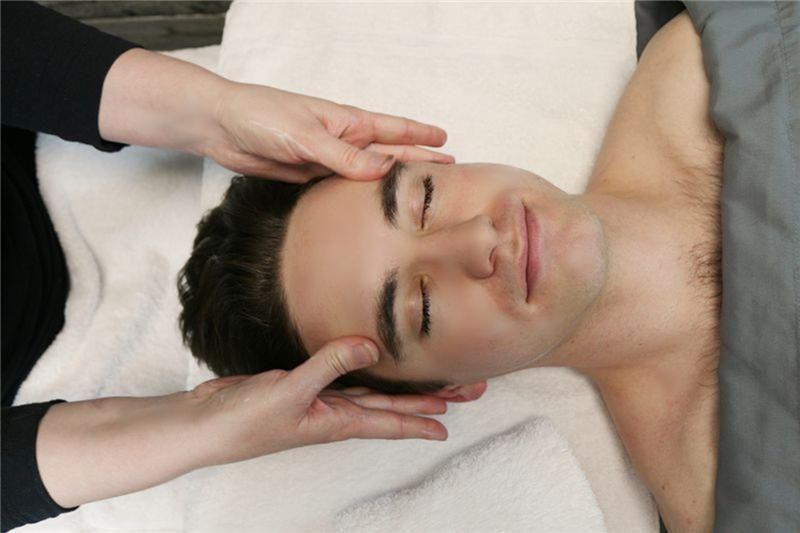 A person lying on a massage table receiving a relaxing facial massage from a practitioner.