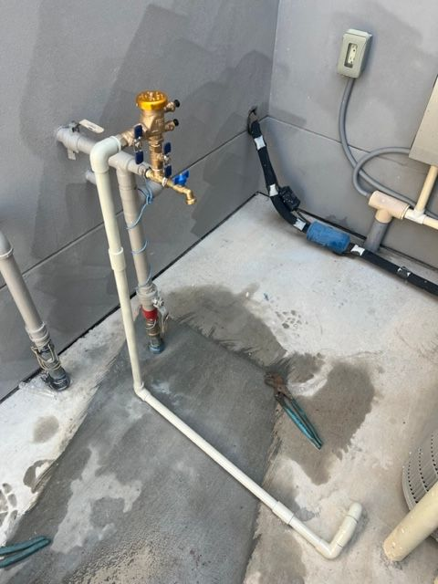 White PVC pipes forming an outdoor water system with a spigot and valve against a gray wall.