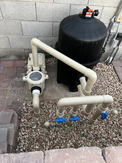 Pool filter and pump system with beige pipes and black filter on gravel.