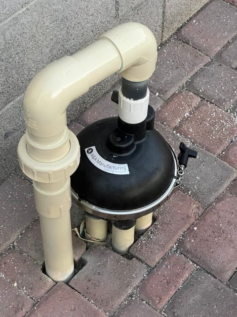 Black pool filter with beige PVC pipes on brick patio.