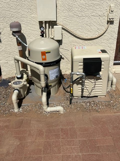 Pool pump, filter, and heater installed outdoors on gravel next to a stucco wall.
