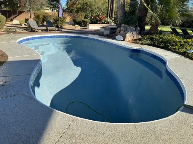 Swimming pool with light blue water and a gray concrete patio, surrounded by landscaping.