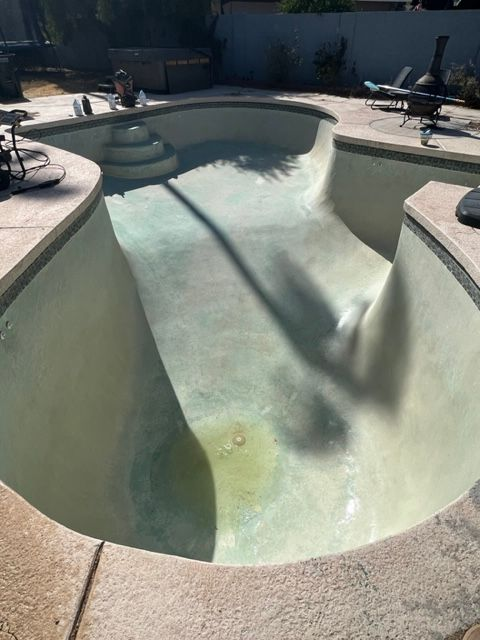 Empty swimming pool with tan-colored walls and a light green bottom, in a sunny outdoor setting.