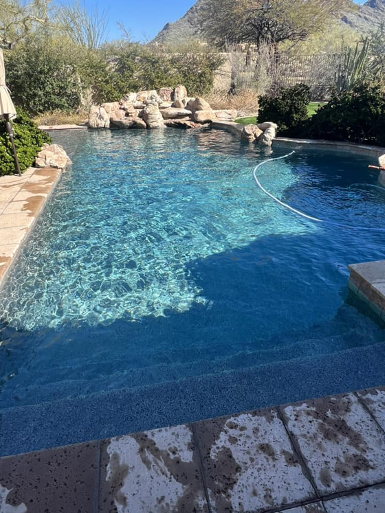 A rectangular swimming pool with clear blue water and stone accents, set against a mountain backdrop.