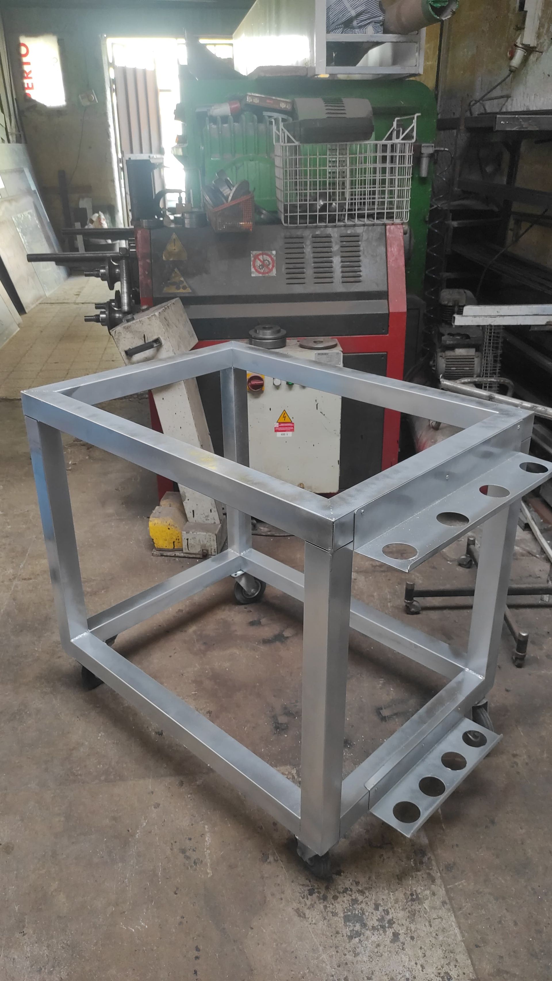 Telaio di carrello in metallo su ruote, con fori per gli utensili, in un ambiente da officina.