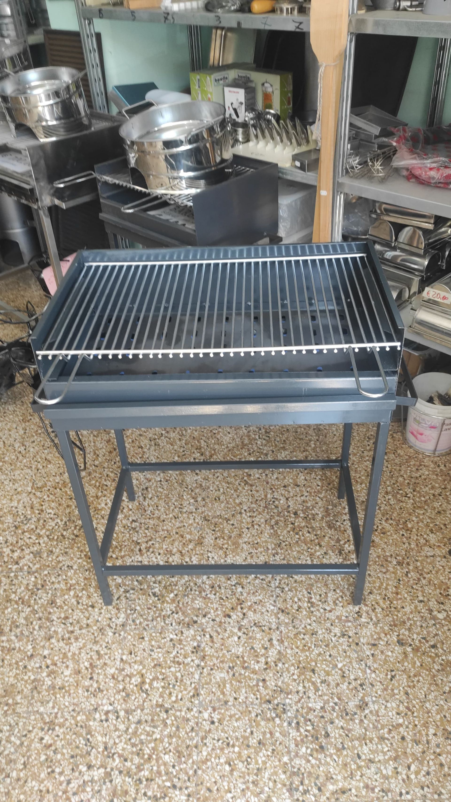 Barbecue in metallo nero con griglia metallica, su un pavimento piastrellato in un negozio.