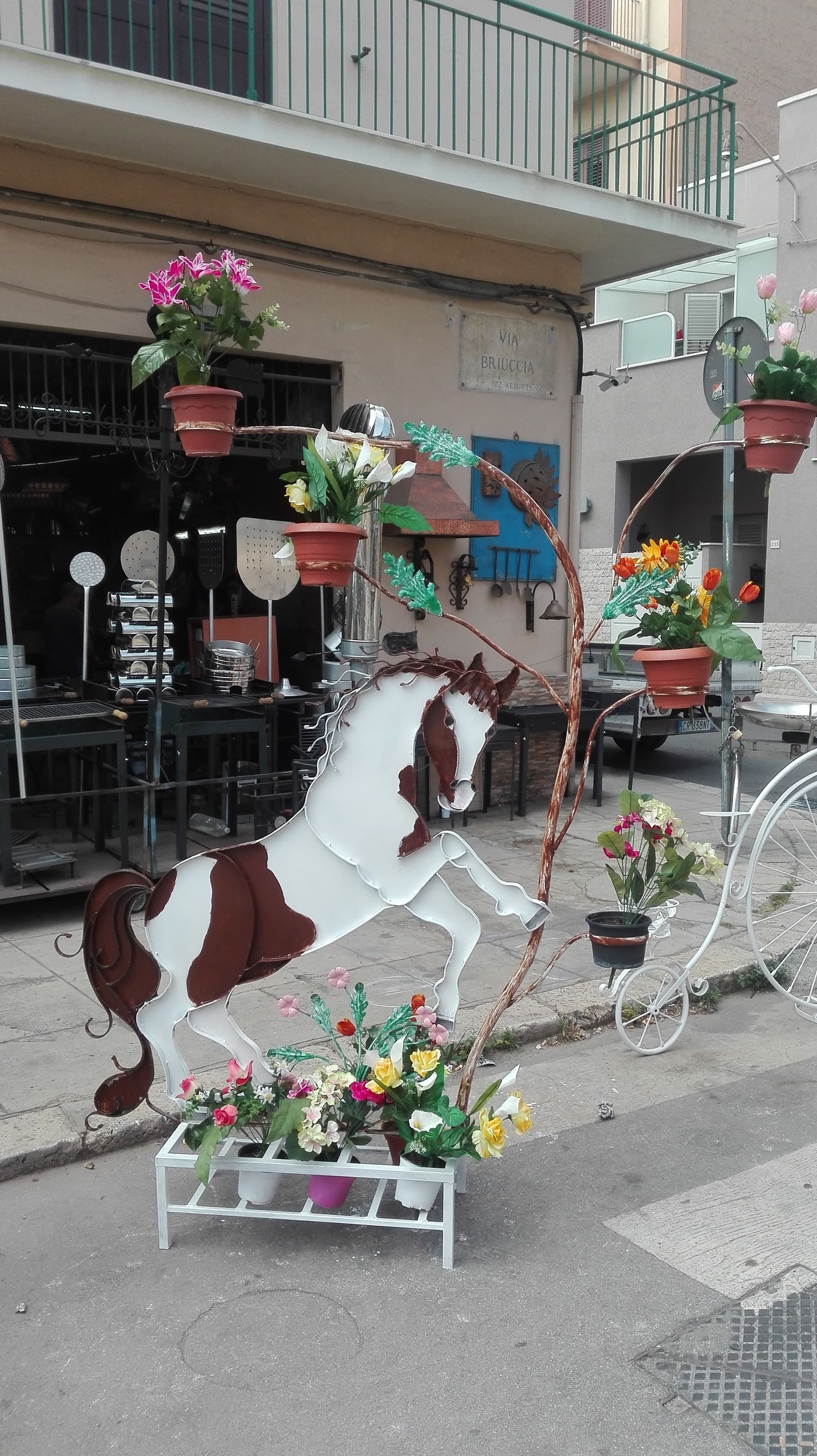Una scultura in metallo raffigurante un cavallo rampante con fiori colorati, esposta su una strada.