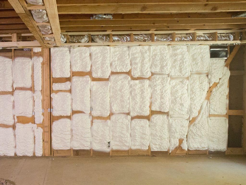 Interior wall with exposed wooden studs and white spray foam insulation.