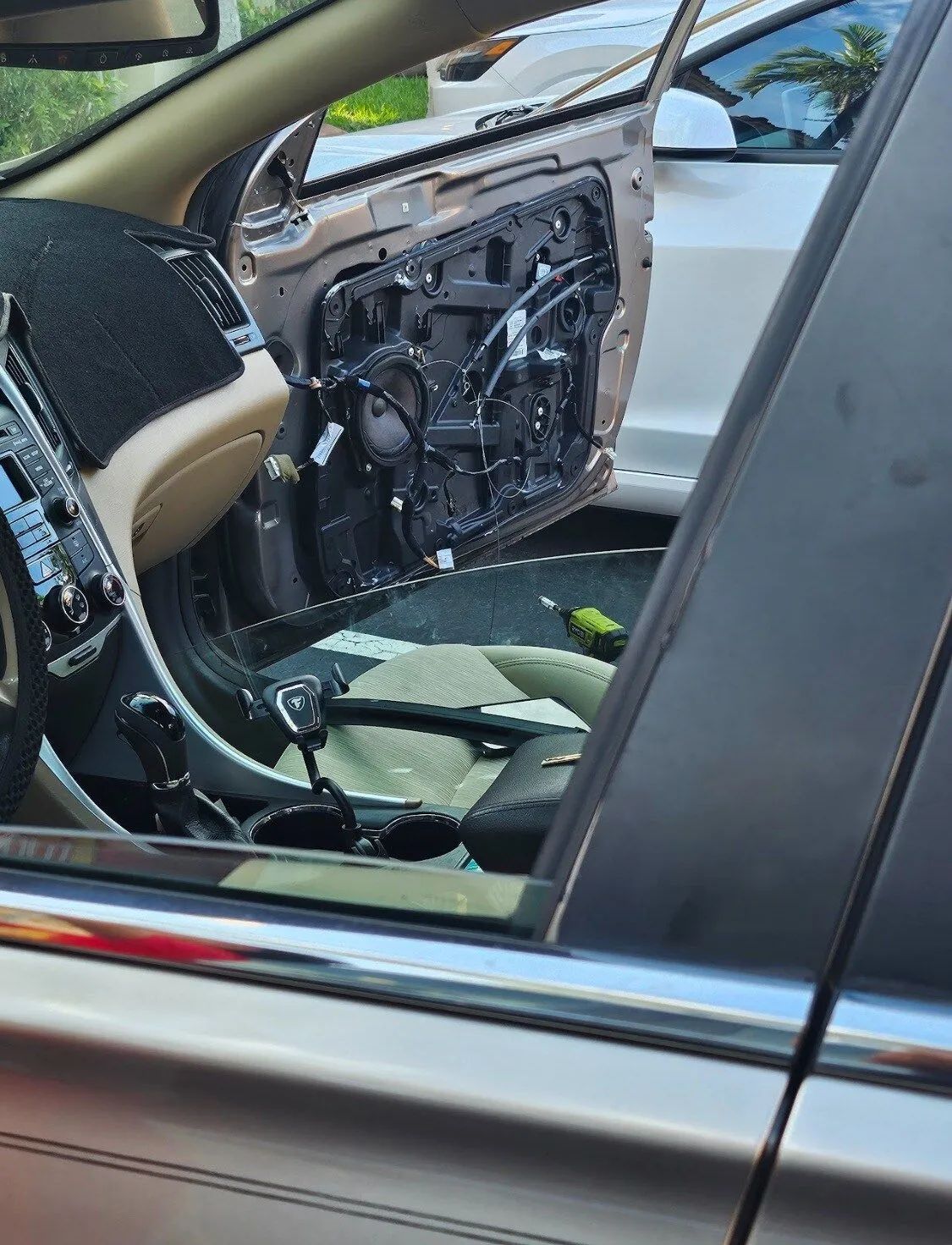Car door interior removed, exposing wiring and broken panel, seen through an open side window.