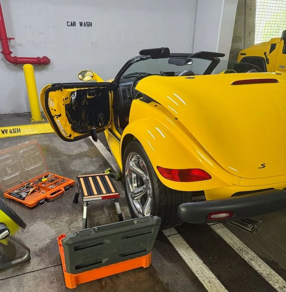Yellow Plymouth Prowler convertible with the door open, tools and work area in a parking garage.