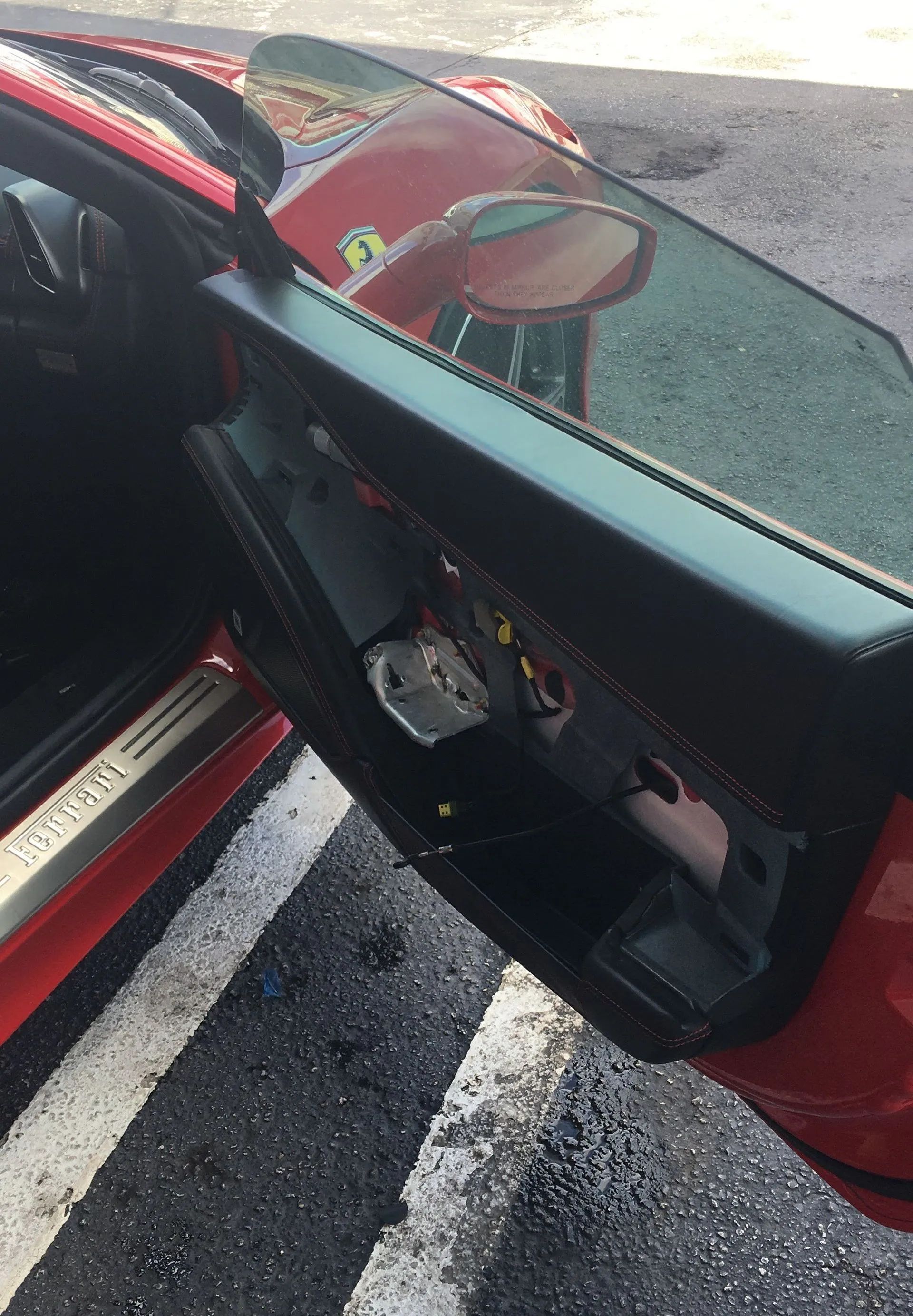 Car door open with damaged interior panel, red exterior, parked on a roadside with white lane markings.