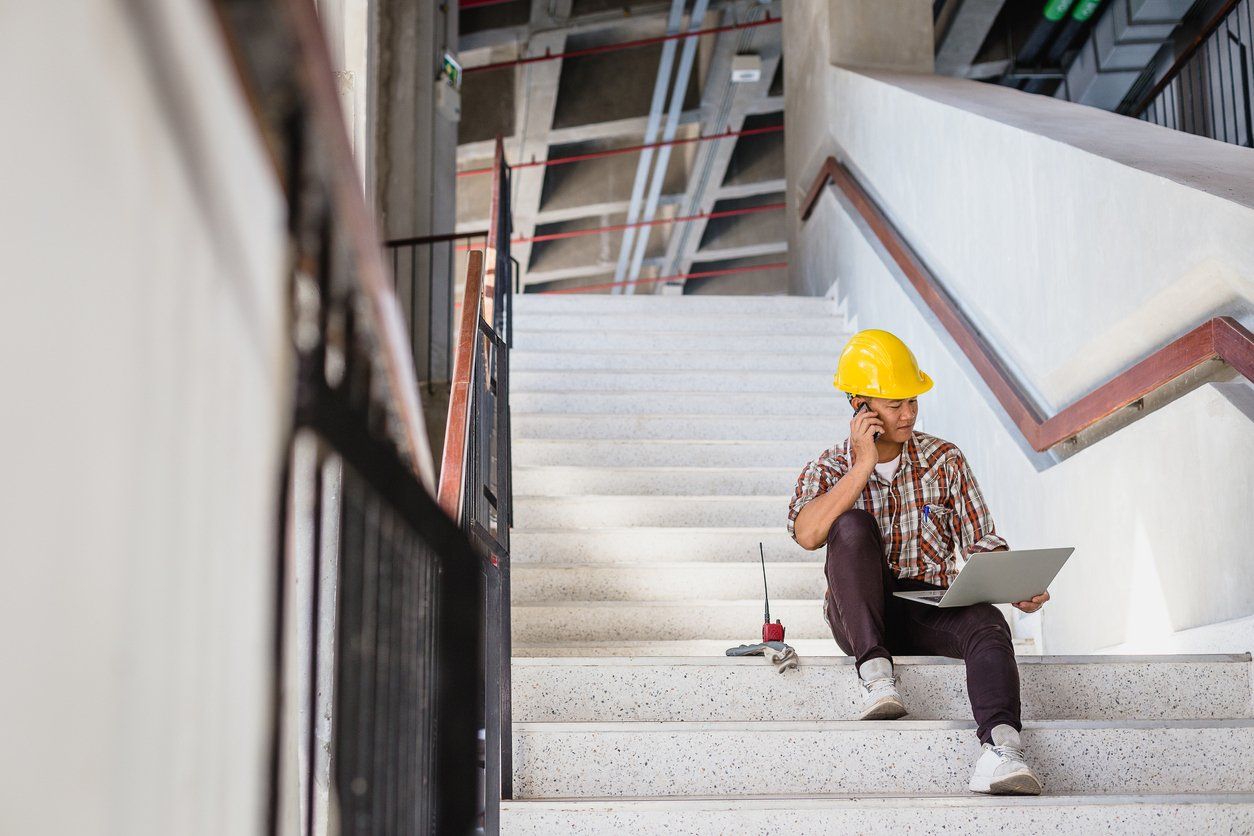 Male electrician speaking on the phone with a client while using a laptop - improving visibility of electrician business website.
