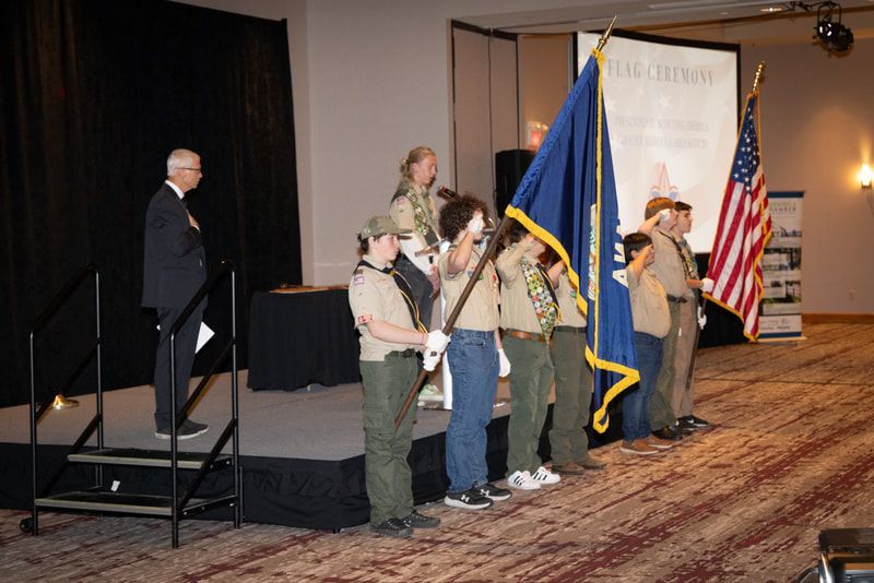 A group of boy scouts are standing on a stage holding flags.