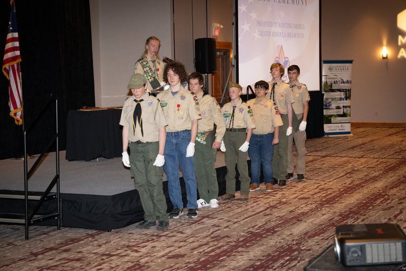 A group of boy scouts are standing on a stage in a room.