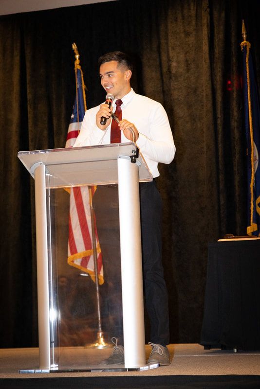 A man is standing at a podium holding a microphone.
