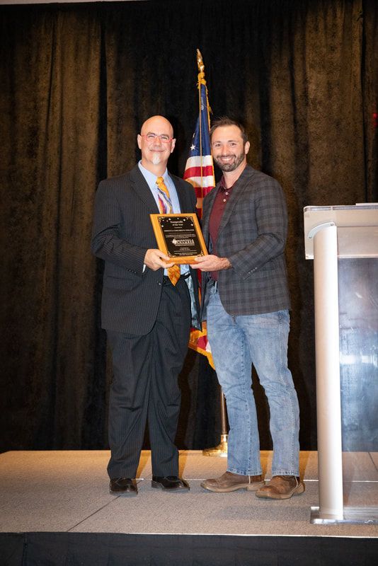 Two men are standing on a stage holding a plaque.
