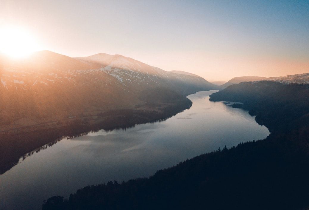 An aerial view of a river surrounded by mountains at sunset.