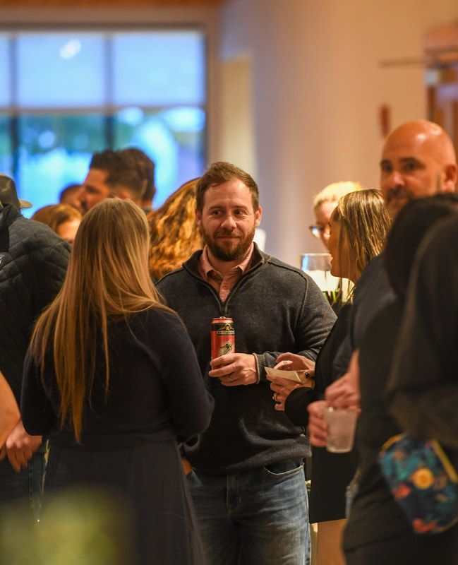 A man with a beard is standing in a crowd of people holding a can of beer.