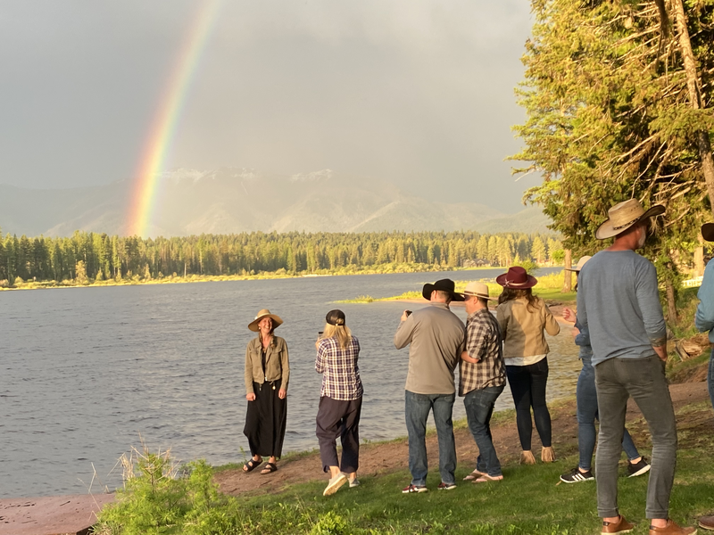 A group of people looking at a rainbow over a lake