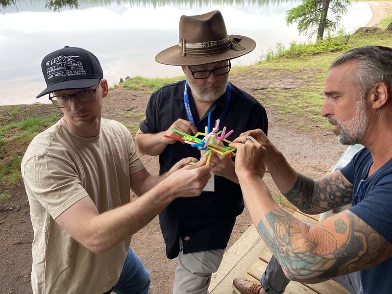 Three men are playing a game on a wooden deck near a lake.