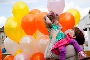 A woman is holding a baby in her arms in front of a bunch of balloons.