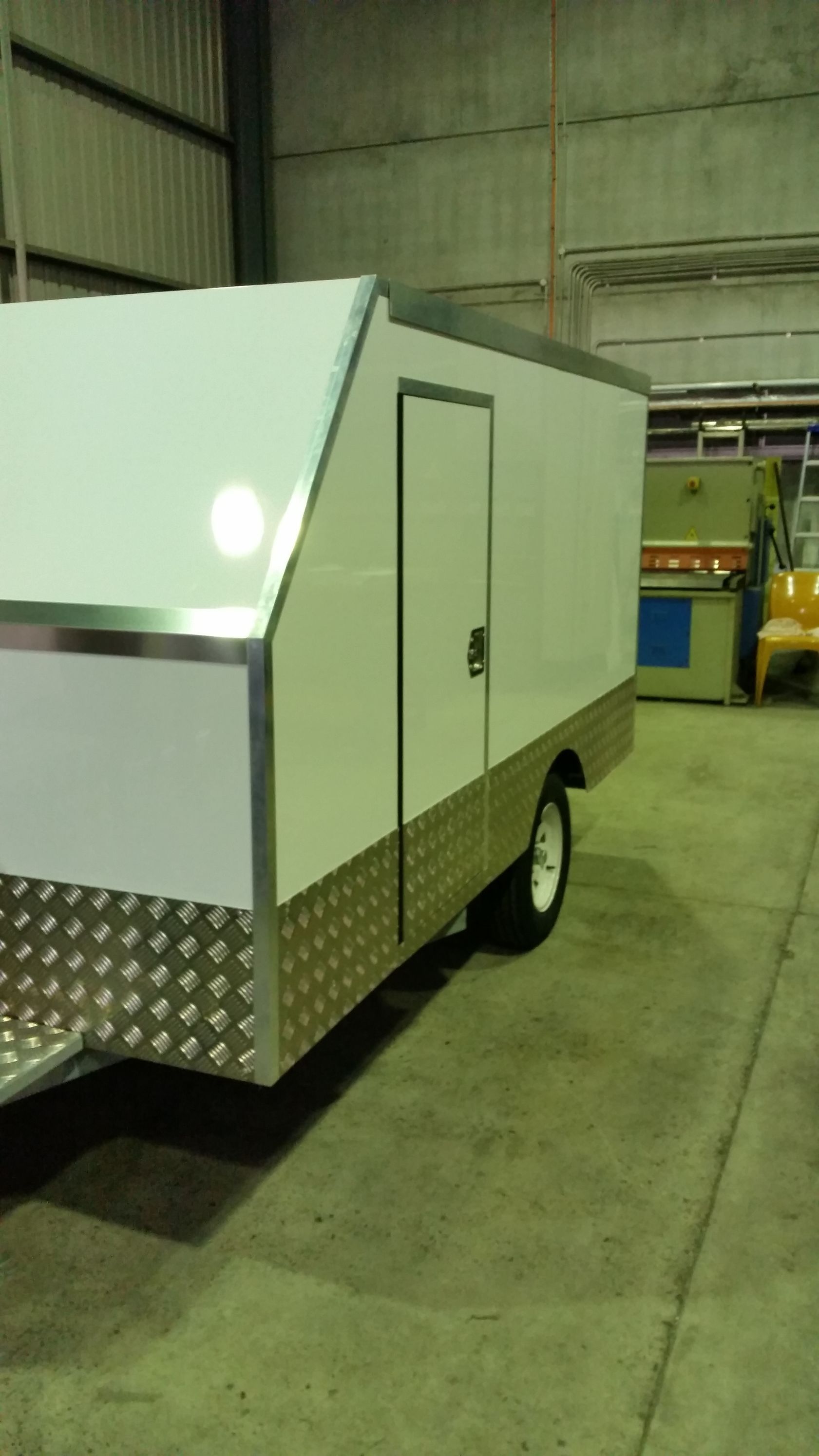 A white trailer is parked in a garage next to a yellow forklift.