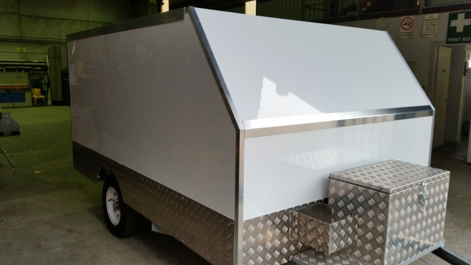 A white trailer with a stainless steel box on the side is parked in a garage.
