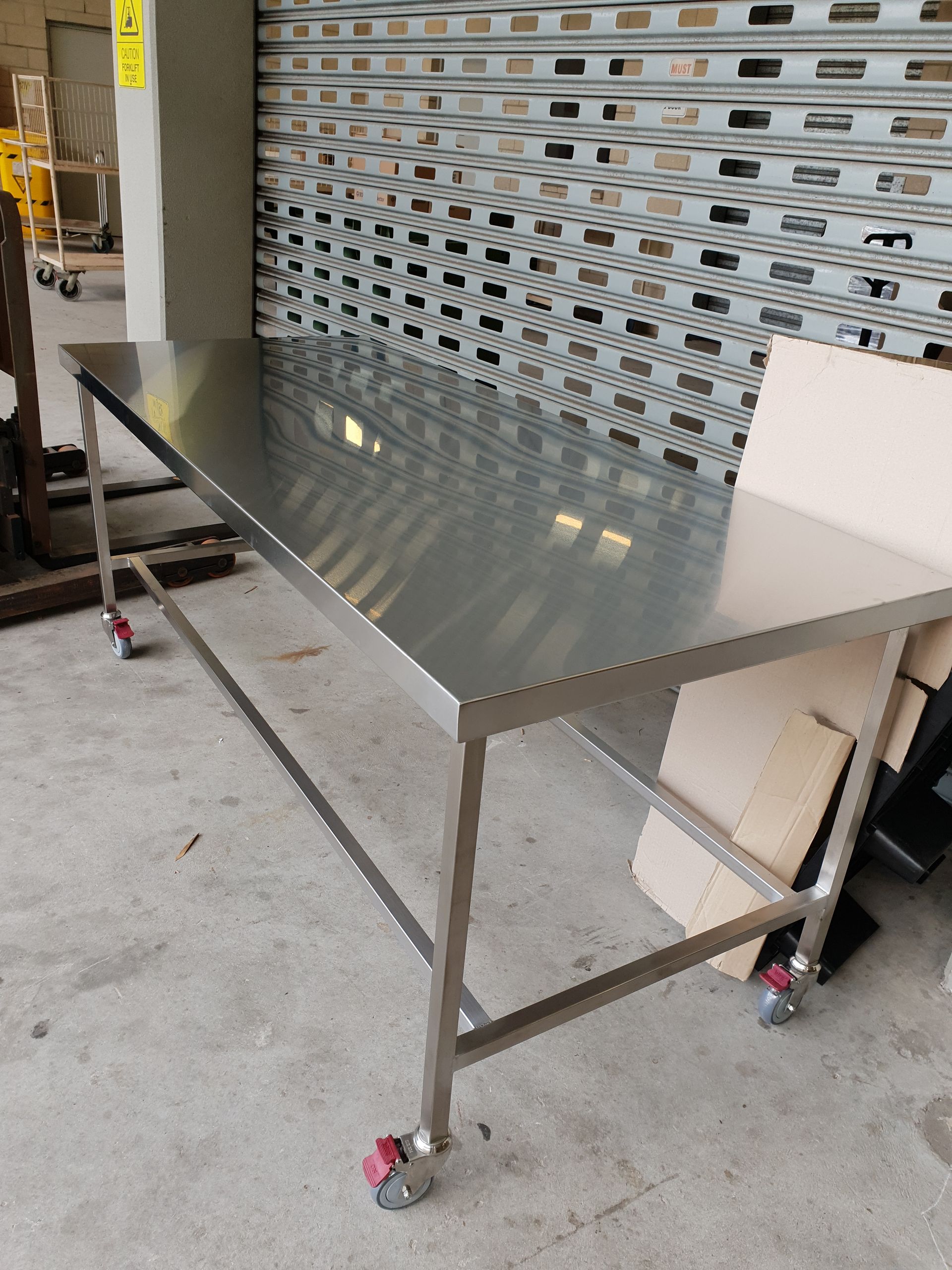 A stainless steel table with wheels is sitting in front of a garage door.