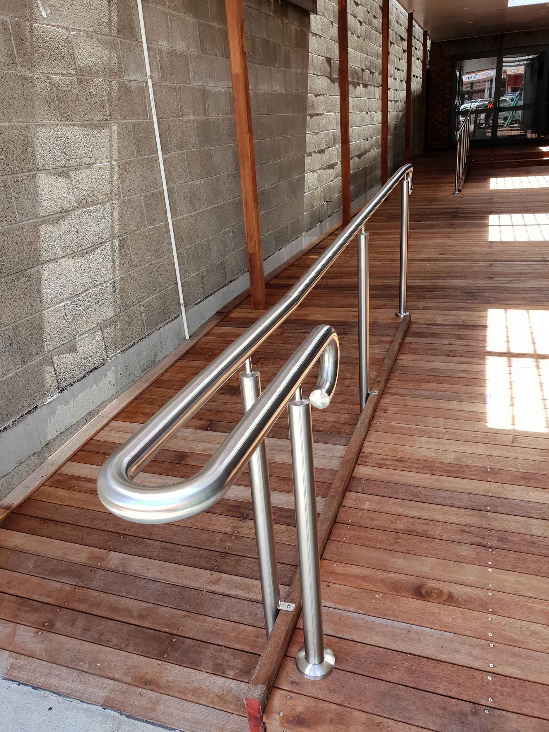 A stainless steel railing on a wooden ramp leading to a building.