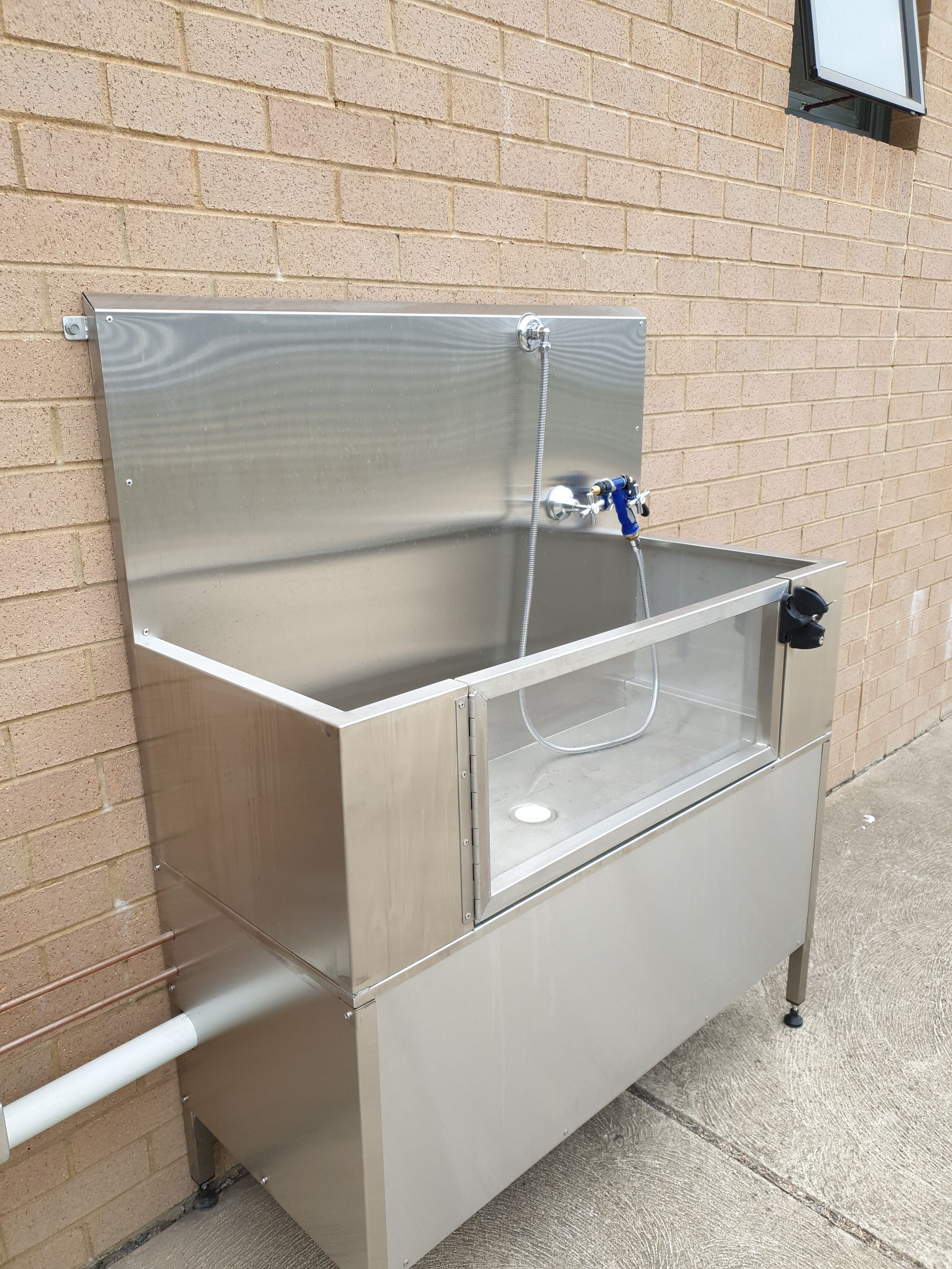 A stainless steel sink is sitting outside of a brick building.