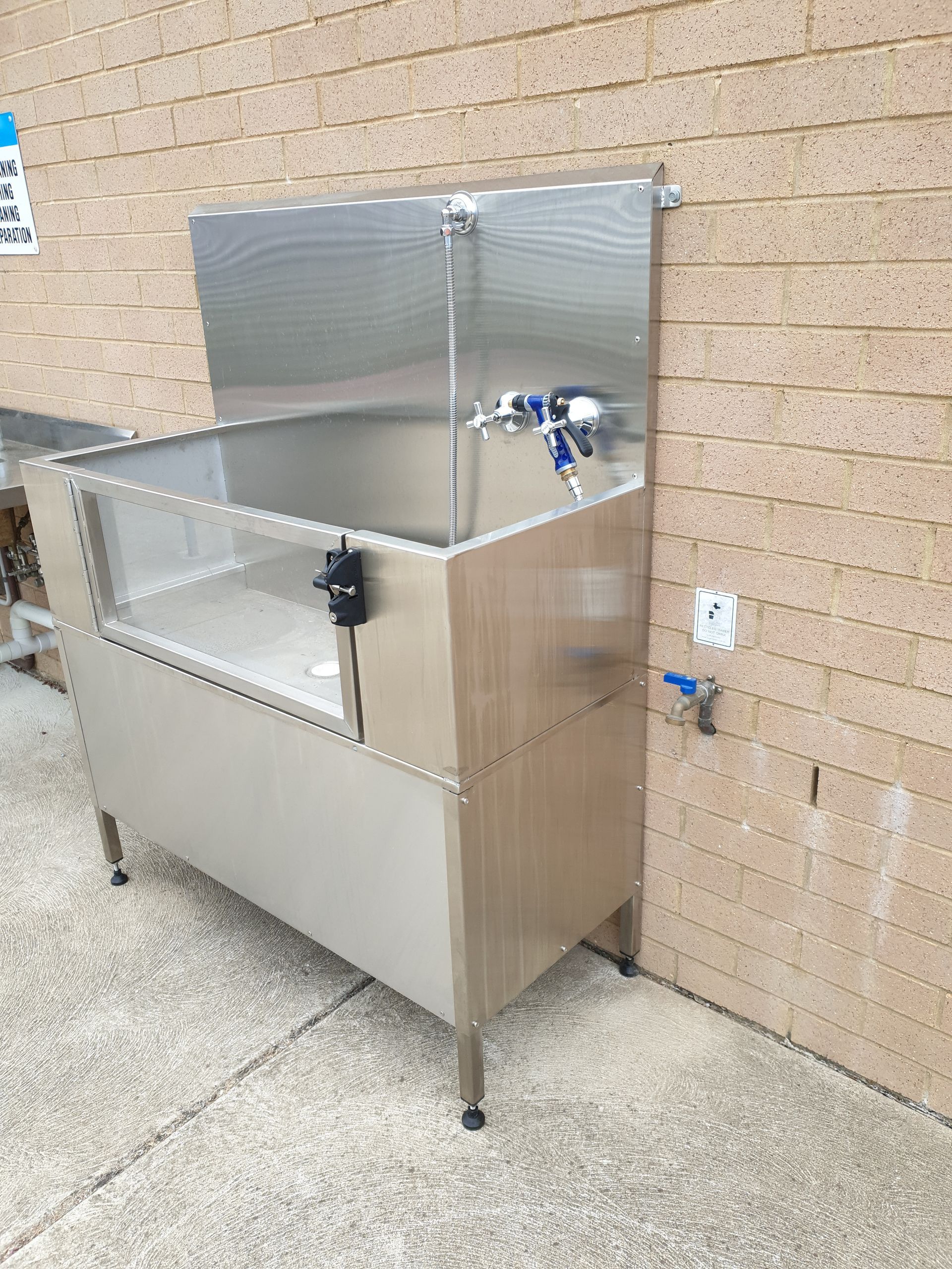 A stainless steel dog bath tub is attached to a brick wall.