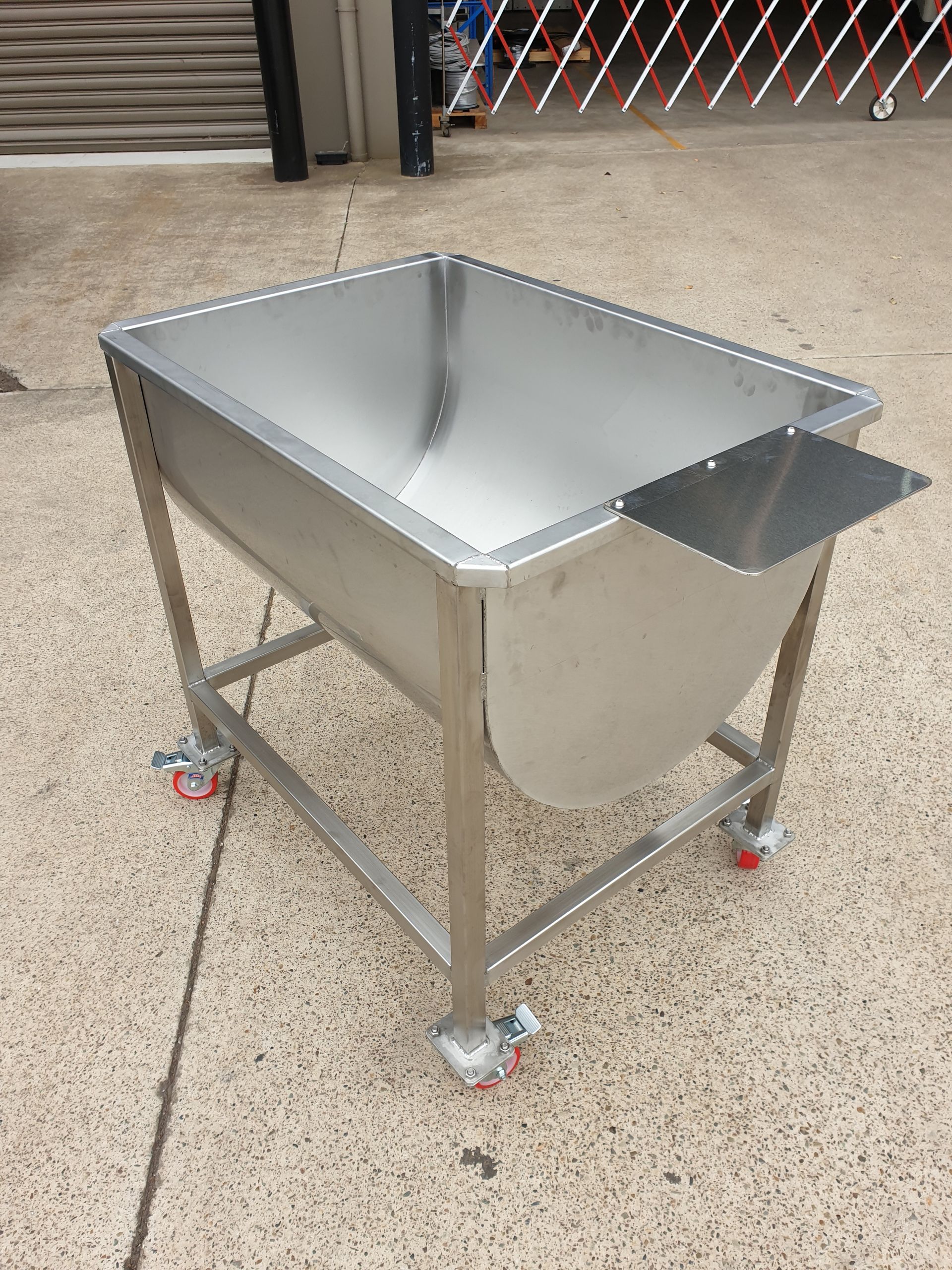 A stainless steel sink on wheels is sitting on the ground.