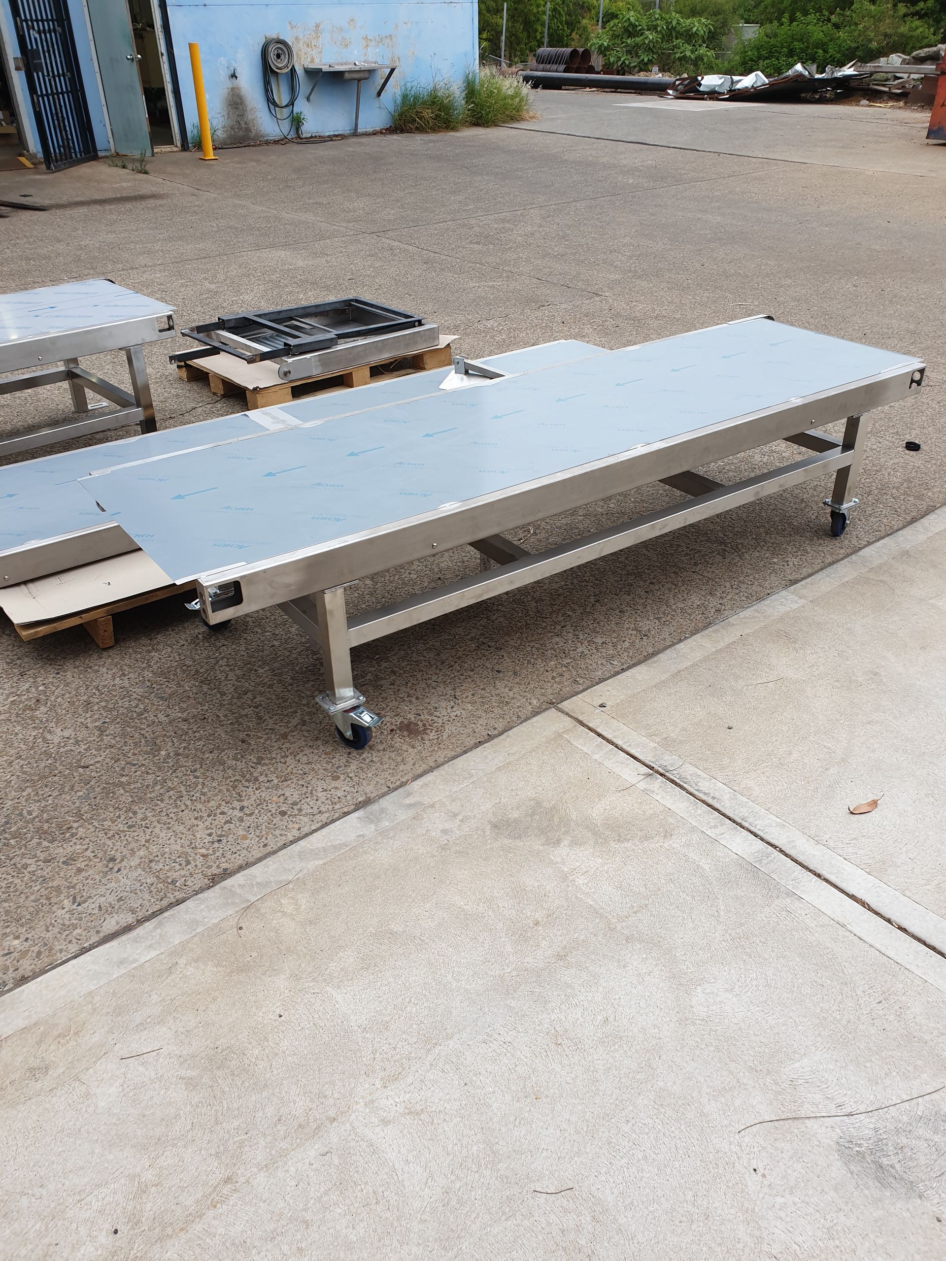 A stainless steel table with wheels is sitting on the ground in a parking lot.