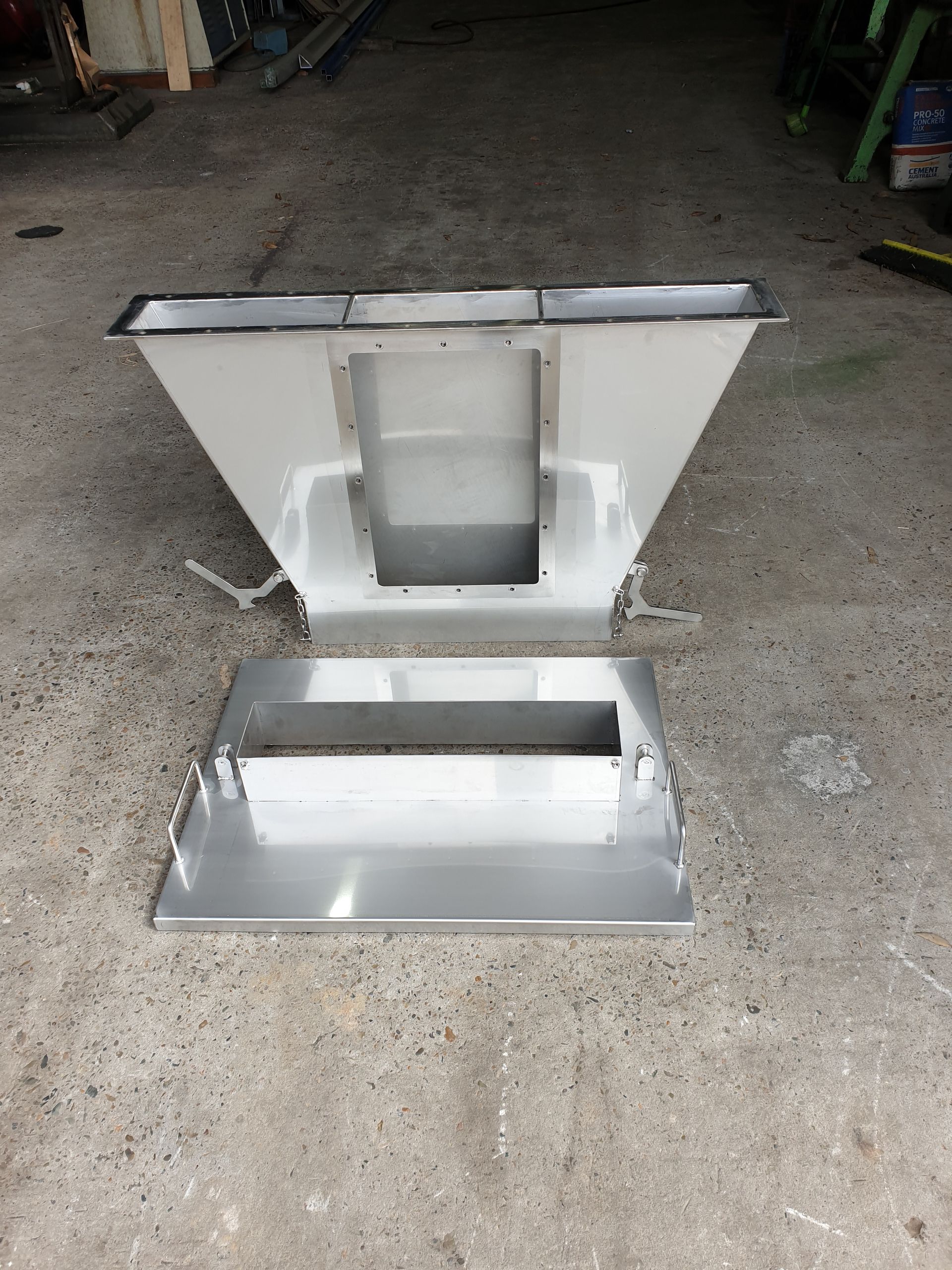 A stainless steel container is sitting on a concrete floor.