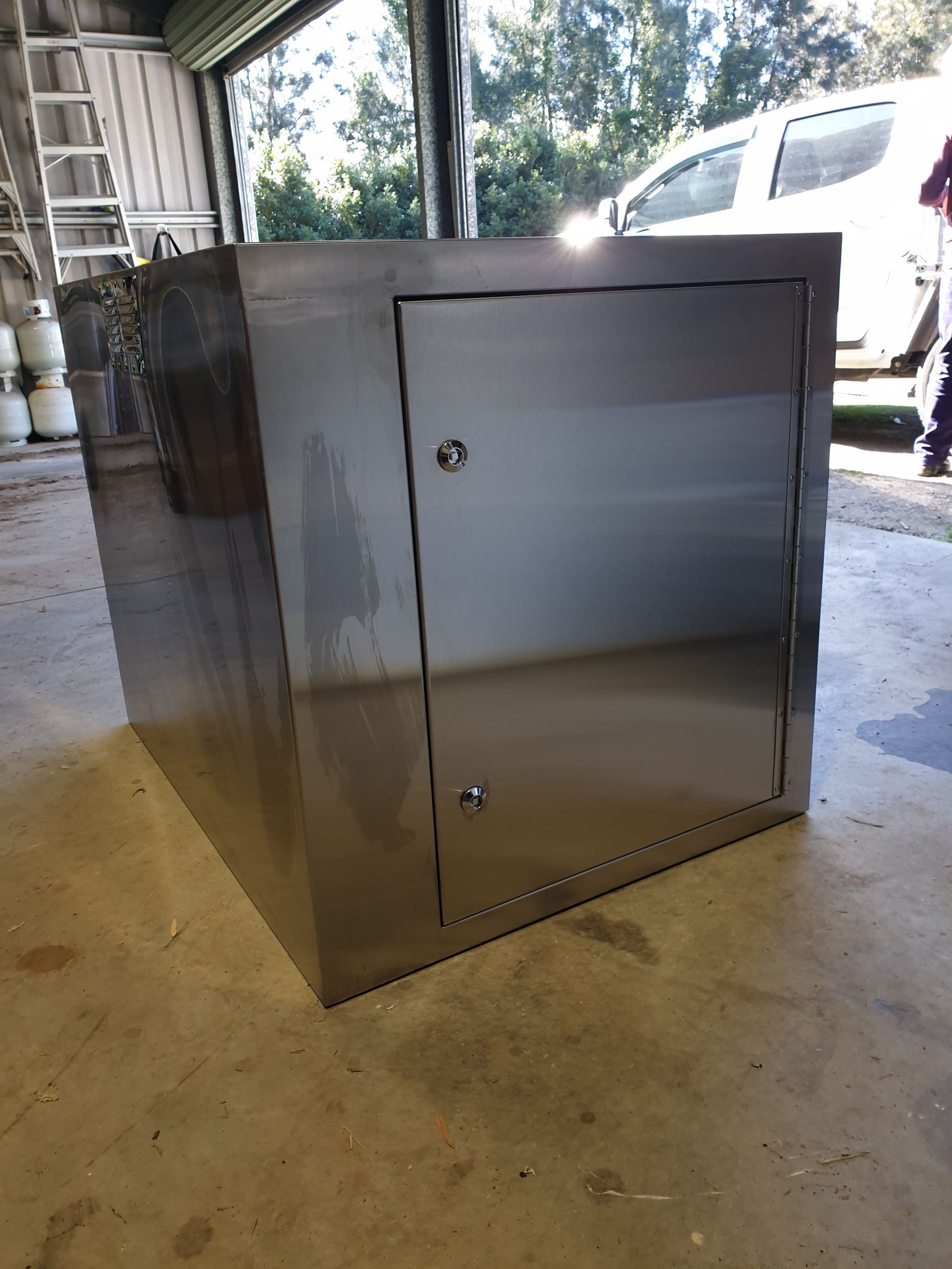 A stainless steel box with a door is sitting on the floor in a garage.