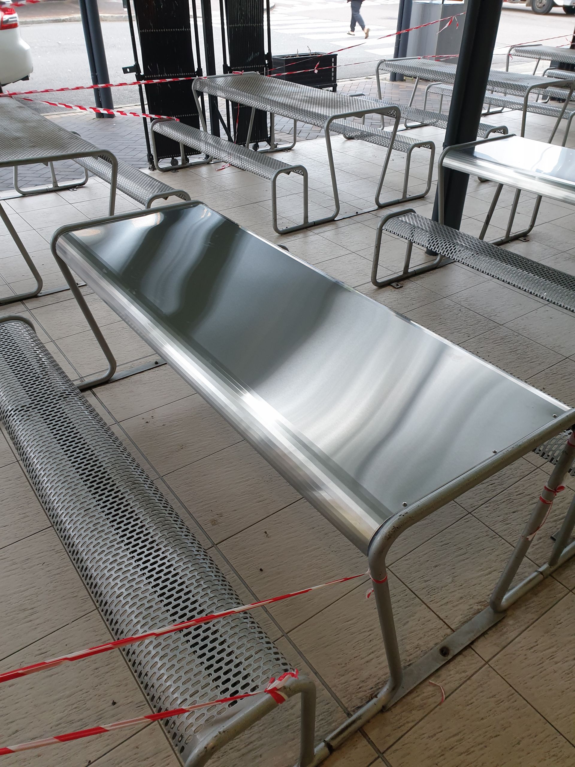 A stainless steel bench is surrounded by other benches and tables