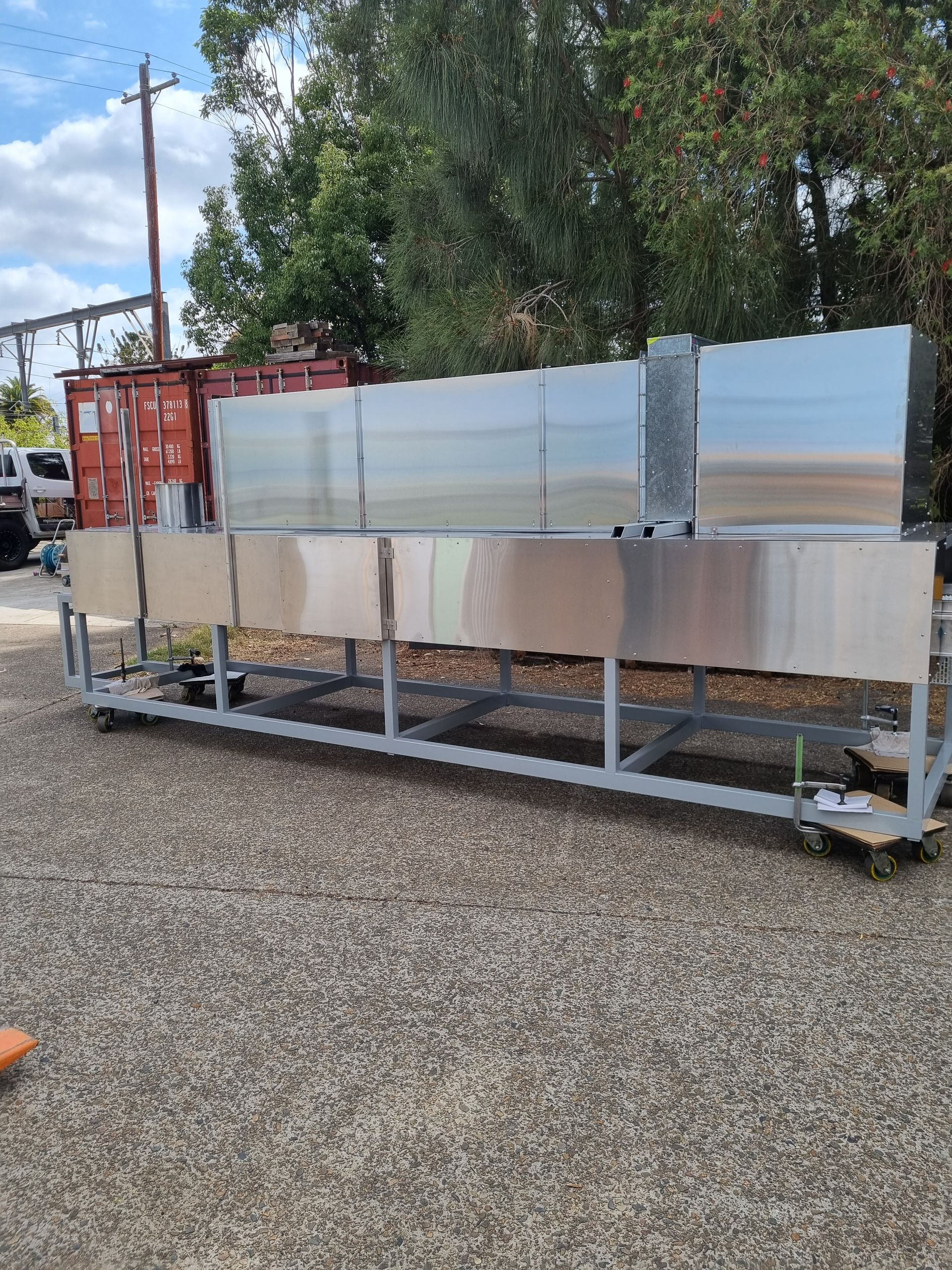 A row of stainless steel sinks are sitting on a cart in a gravel lot.