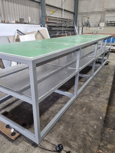 A large metal table with a green top is sitting in a warehouse.