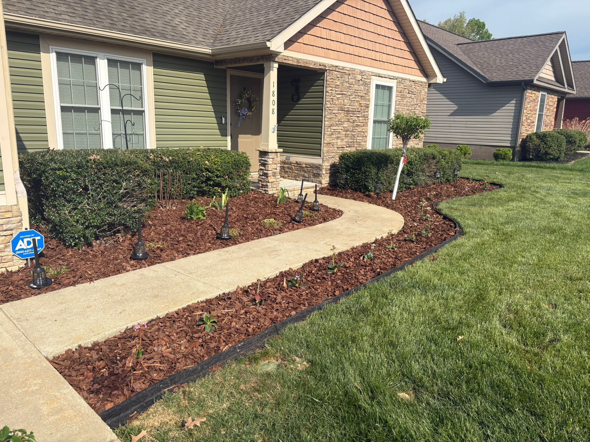 Front yard of a brick house with a curved concrete walkway and mulched garden beds.