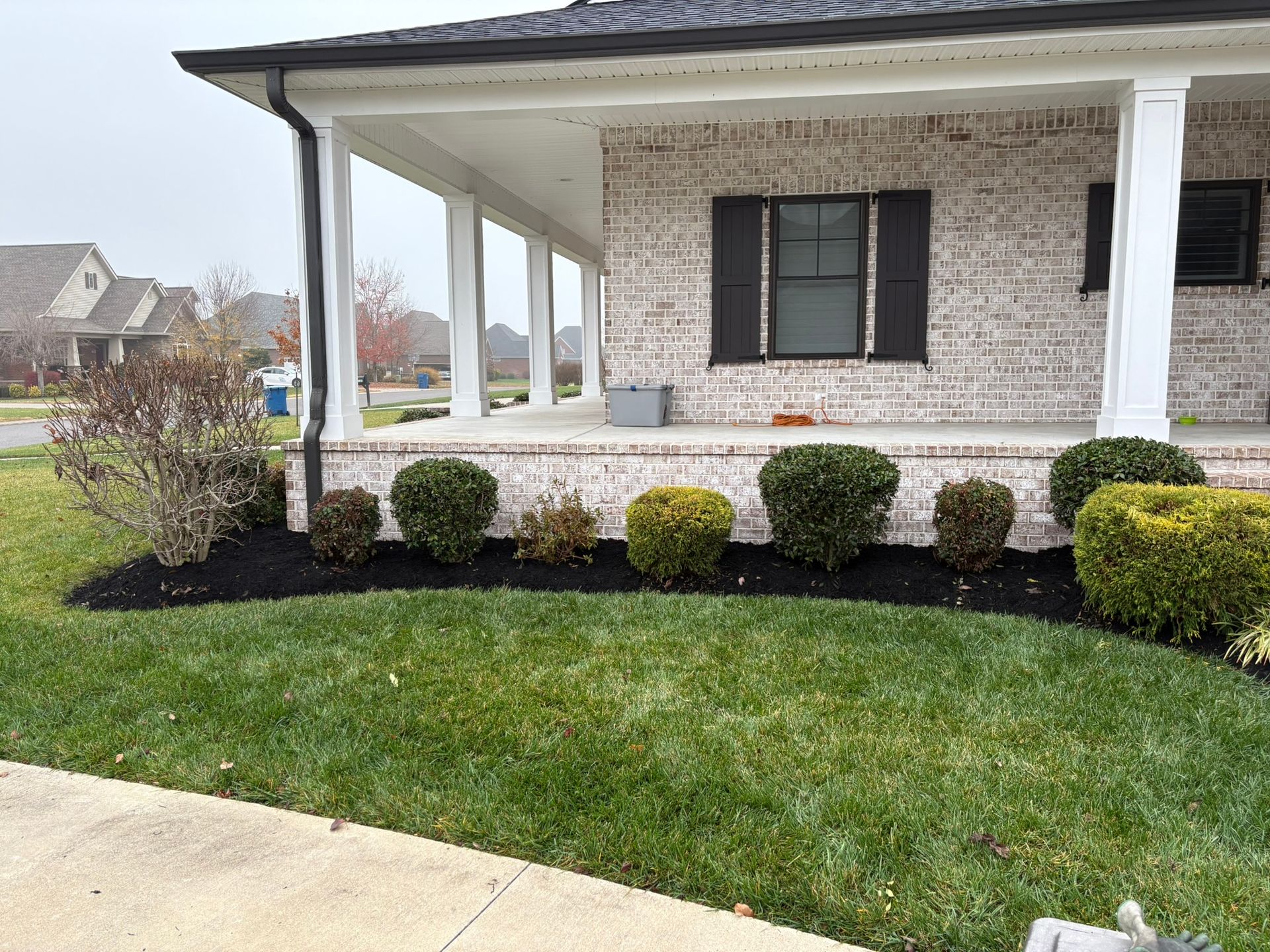 Brick house front porch with trimmed shrubs and a green lawn beside a concrete driveway