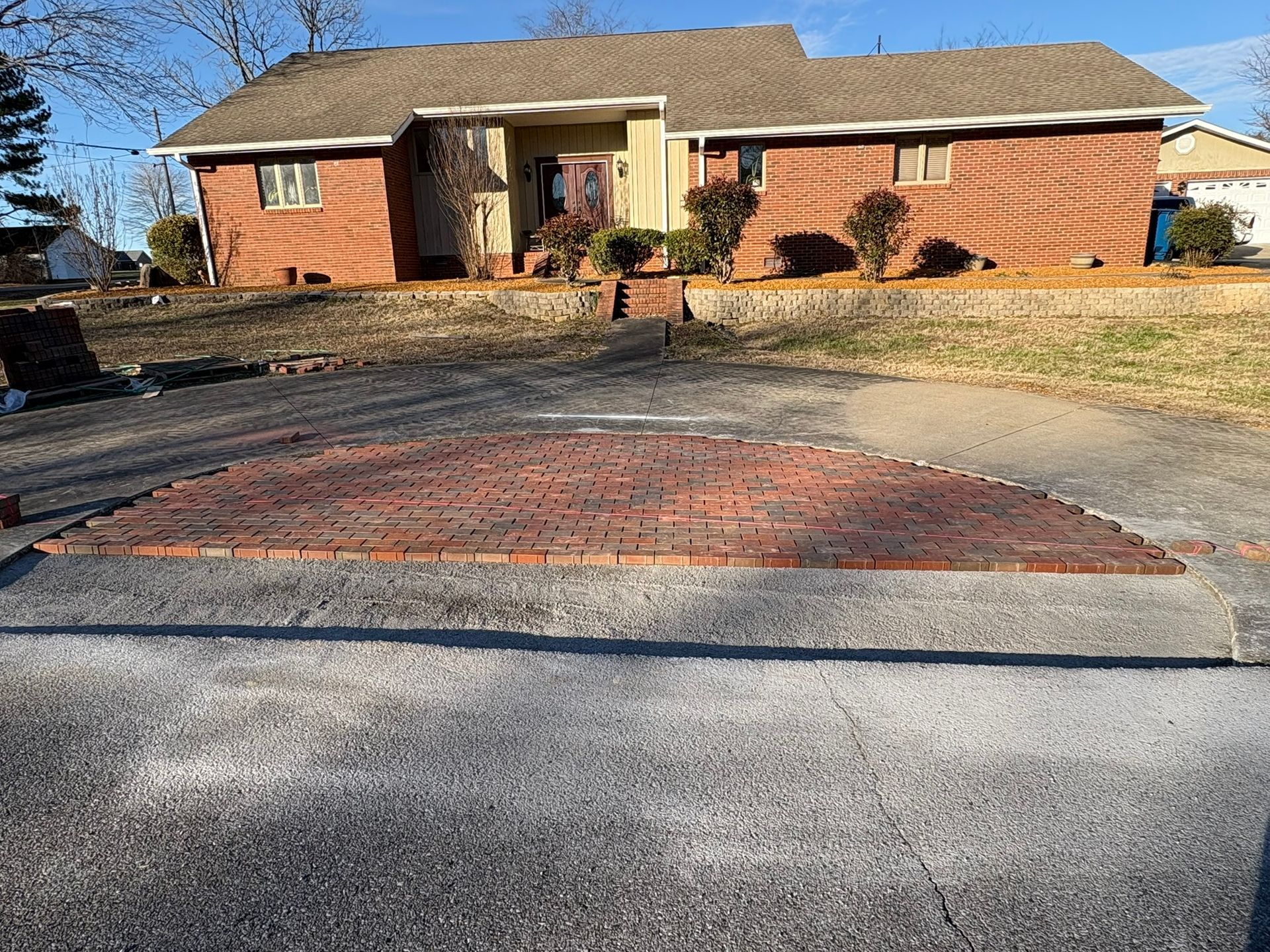 Residential driveway with a brick house and a brick-paved apron, viewed from the street.