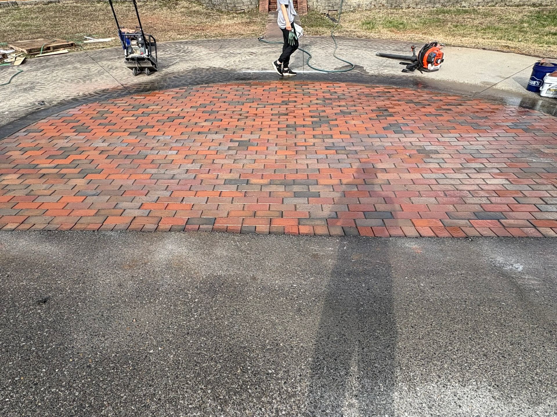 Workers installing a red brick walkway over a gray asphalt surface