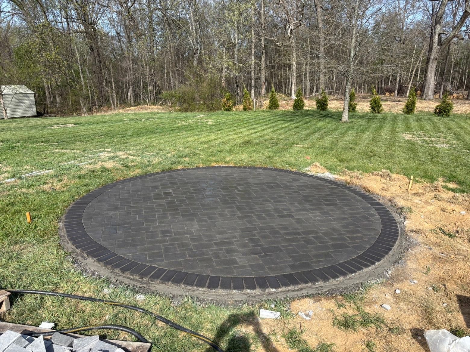 Round black patio pad in a grassy yard with trees in the background